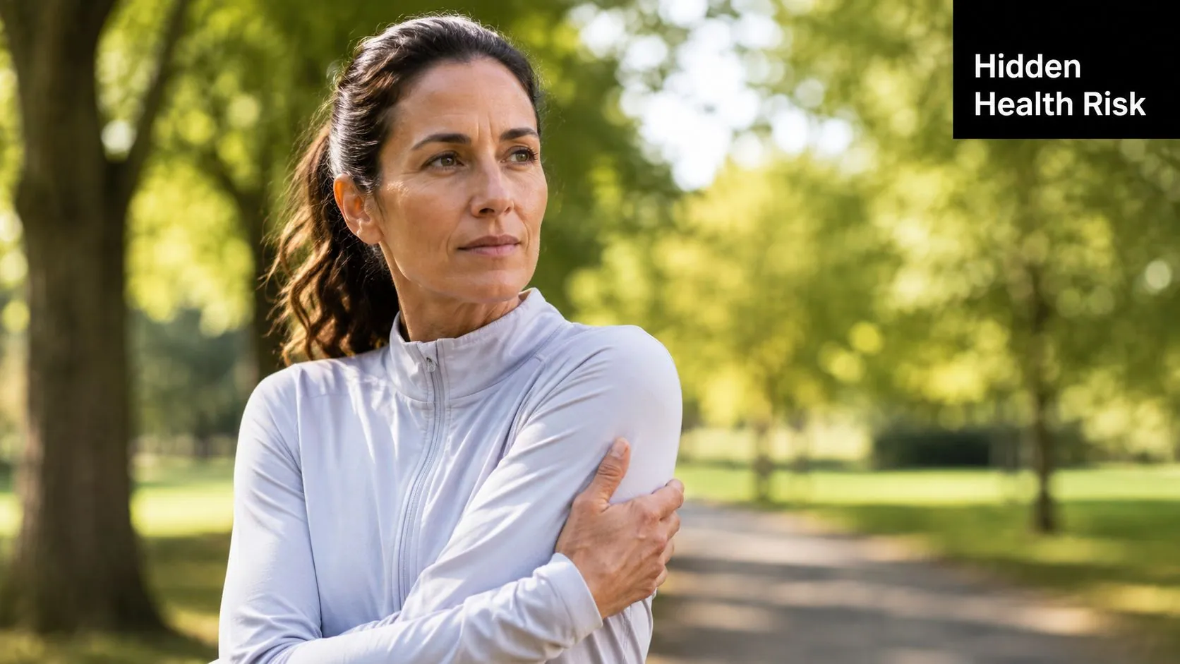 A middle-aged woman in athletic wear looks thoughtful while standing in a park setting.